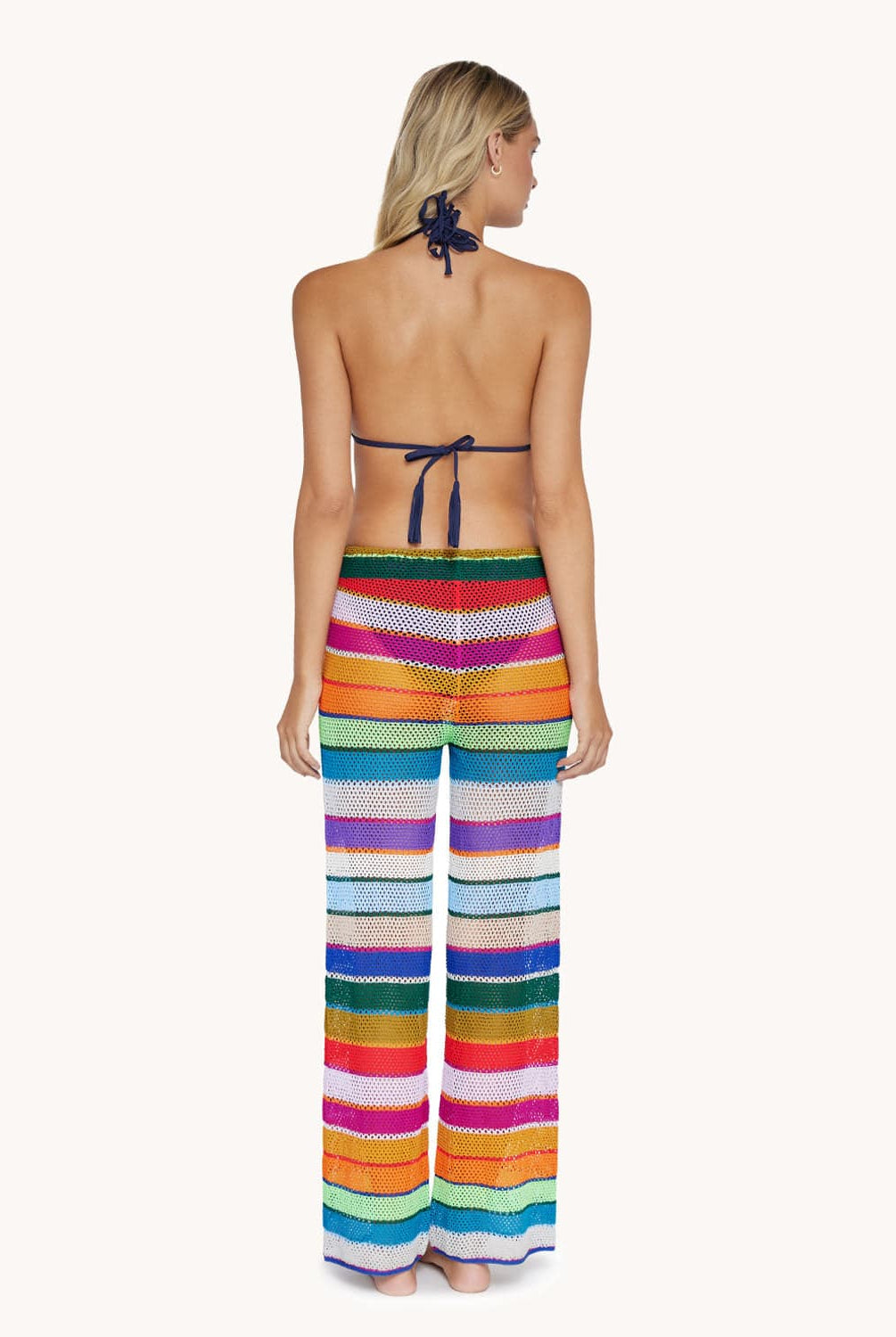 A blonde woman wearing a bikini top and color block pants facing towards a white wall.