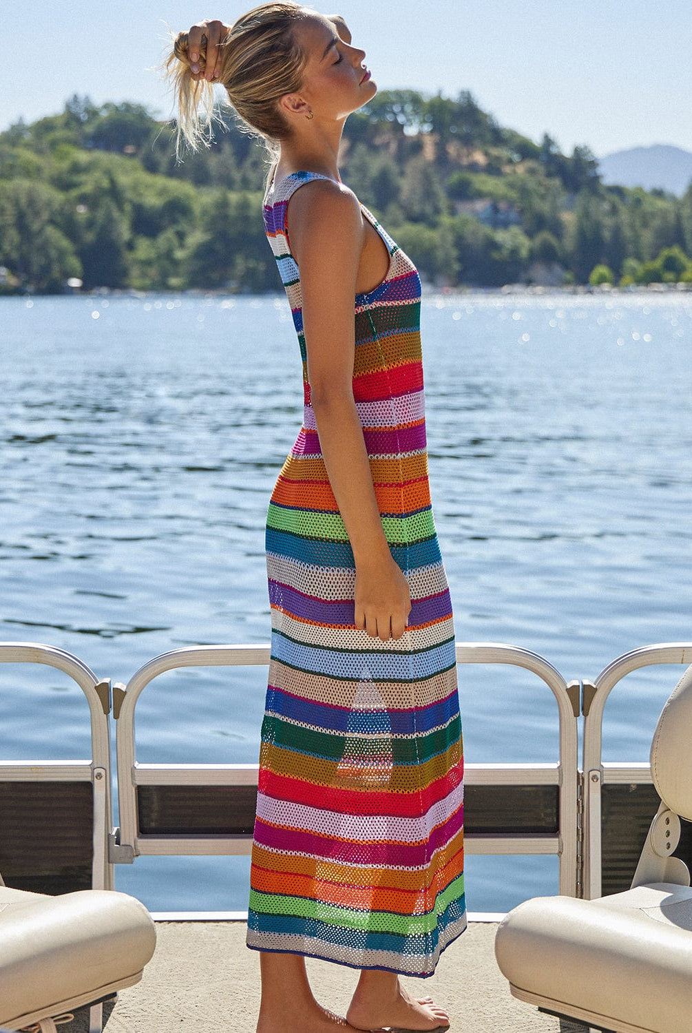 A blonde woman wearing a color block dress standing on a boat on a lake.