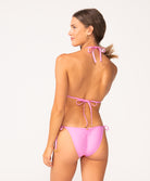 A woman wearing a pink bikini facing towards a white wall.