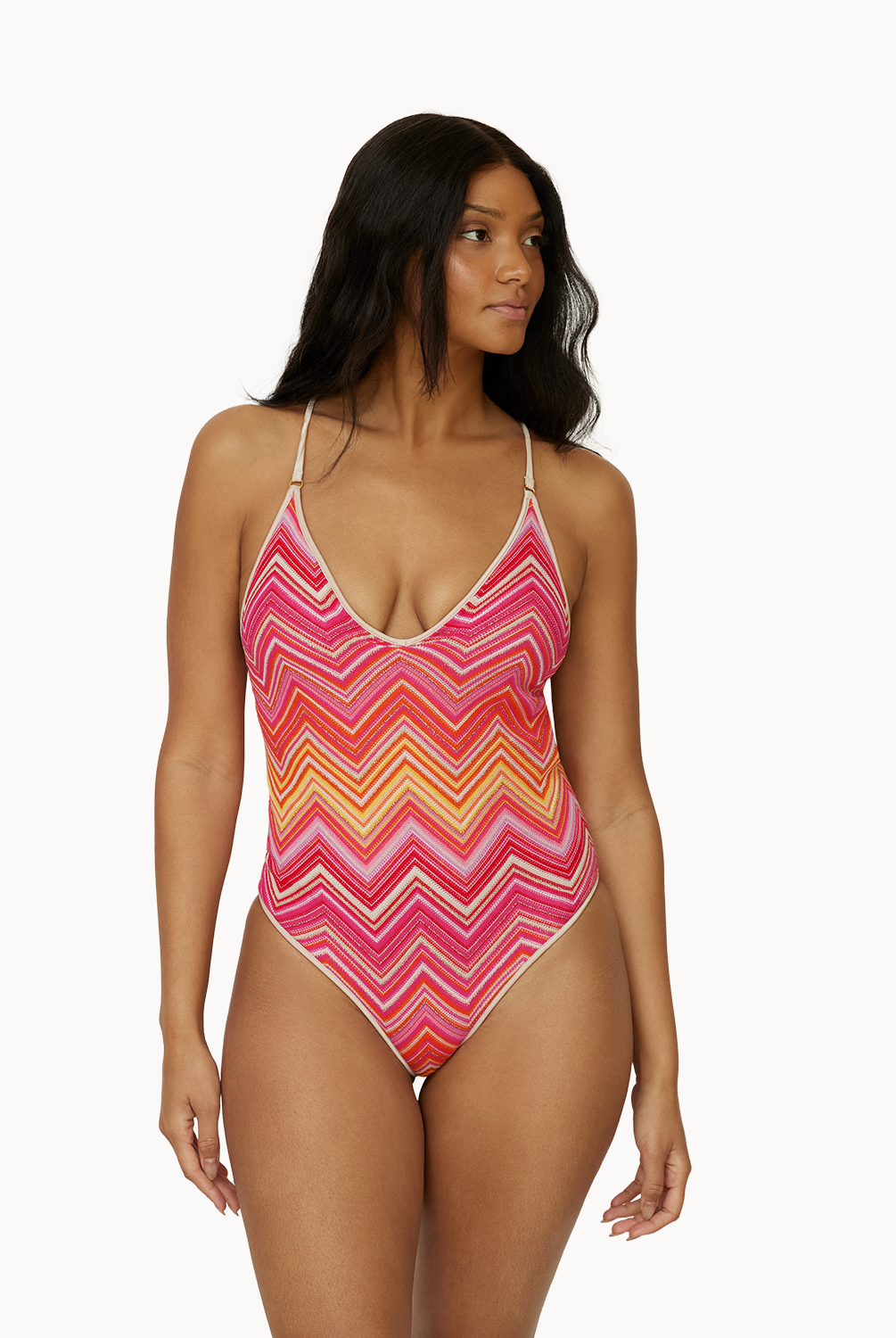 A woman wearing a pink and orange stripe one piece swim suit standing in front of a white wall.
