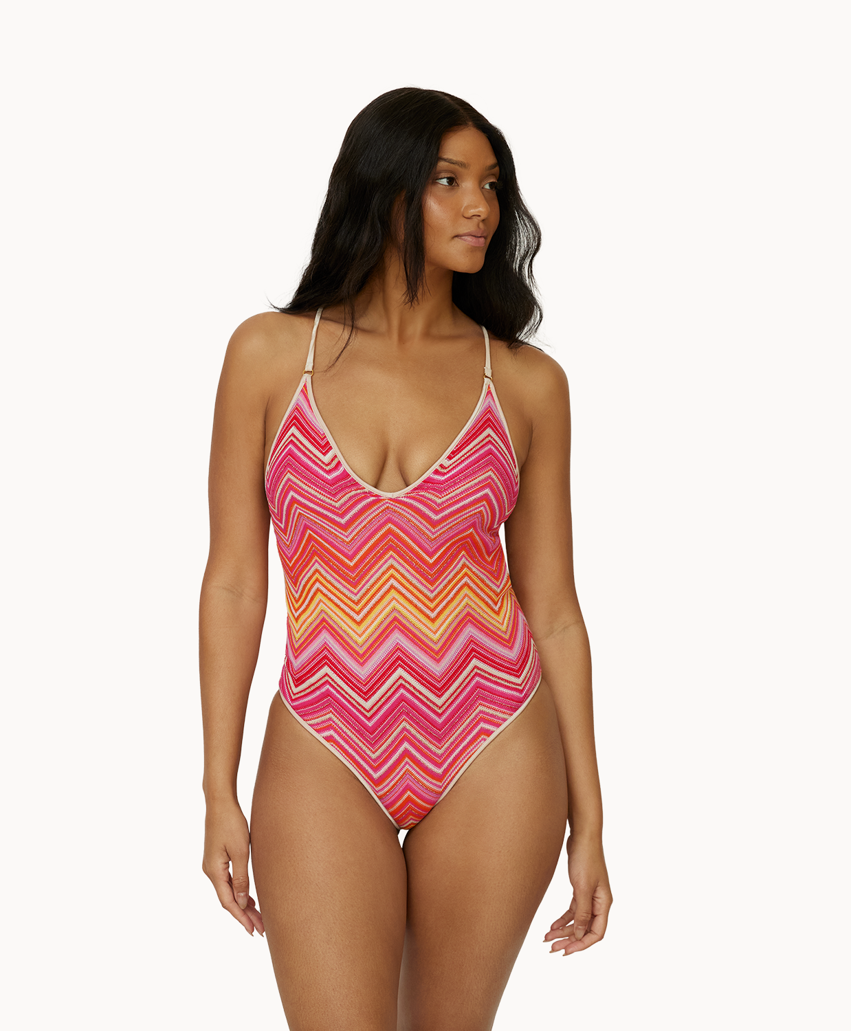 A woman wearing a pink and orange stripe one piece swim suit standing in front of a white wall.