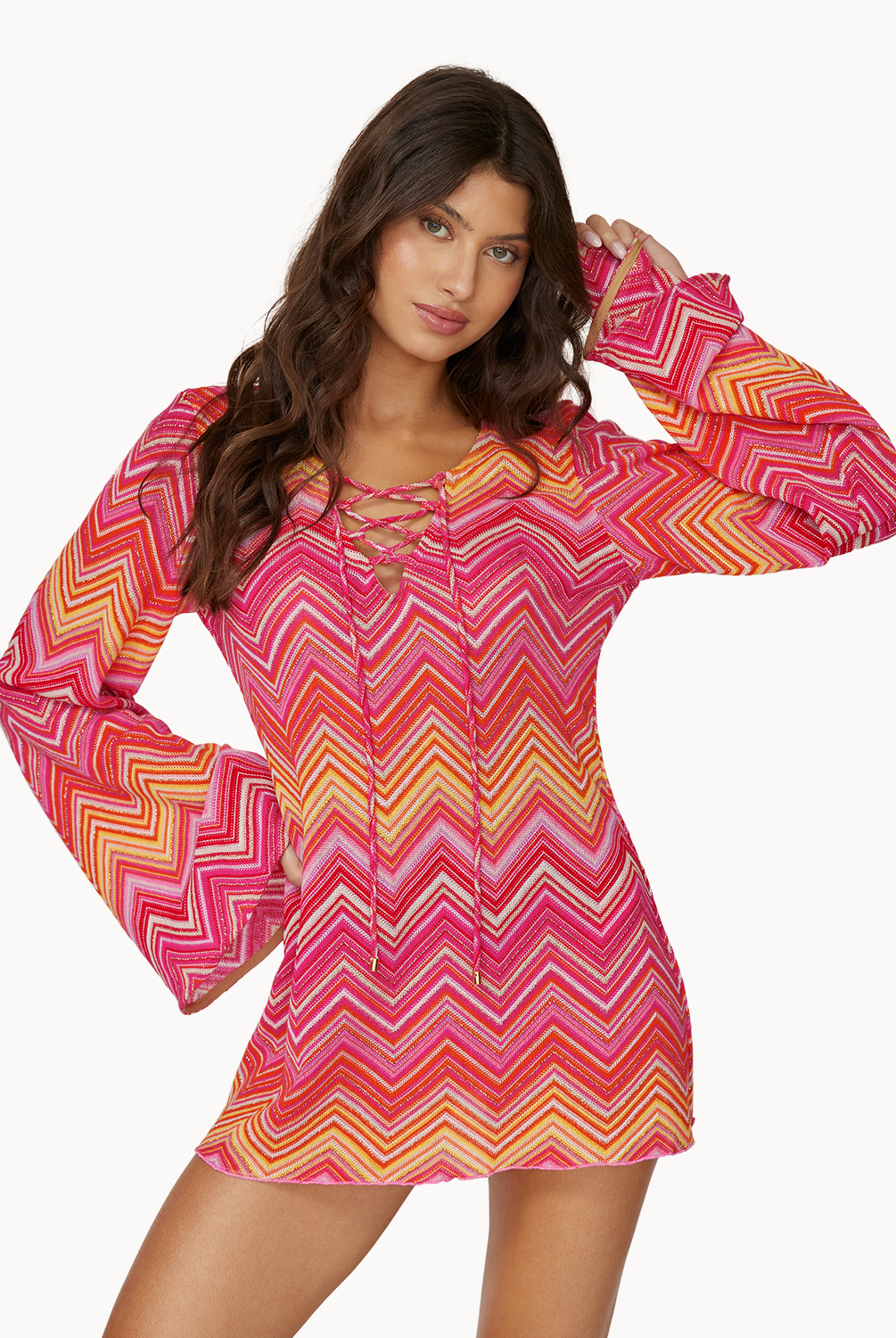 A woman wearing a pink and orange stripe long sleeve dress dress standing in front of a white wall.