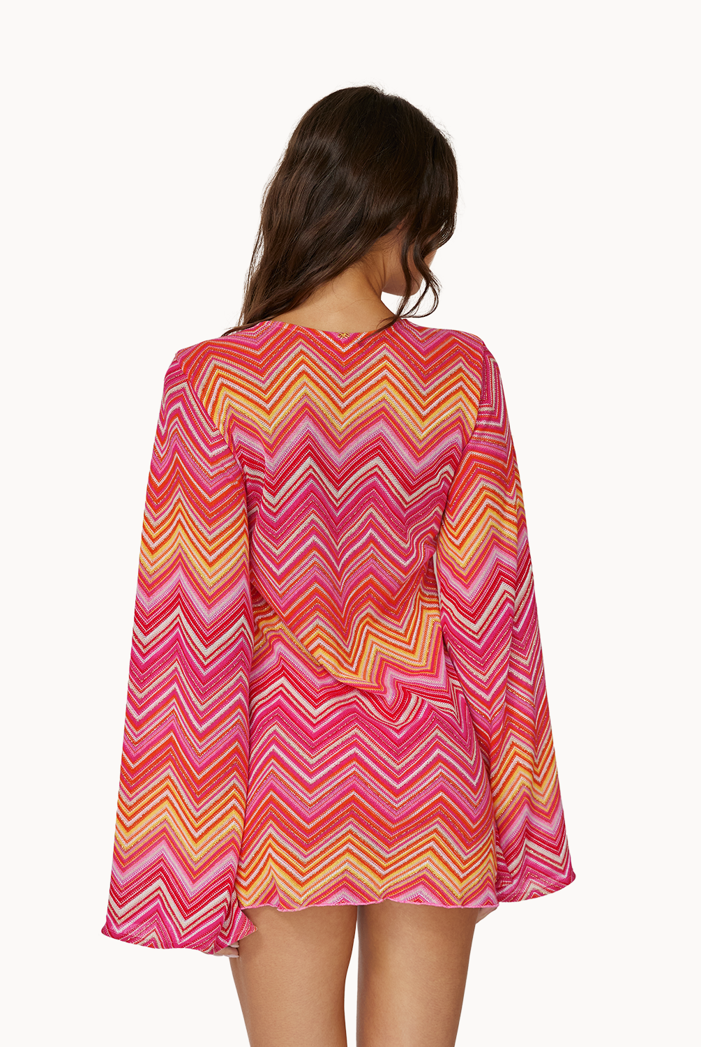A woman wearing a pink and orange stripe long sleeve dress facing a white wall.