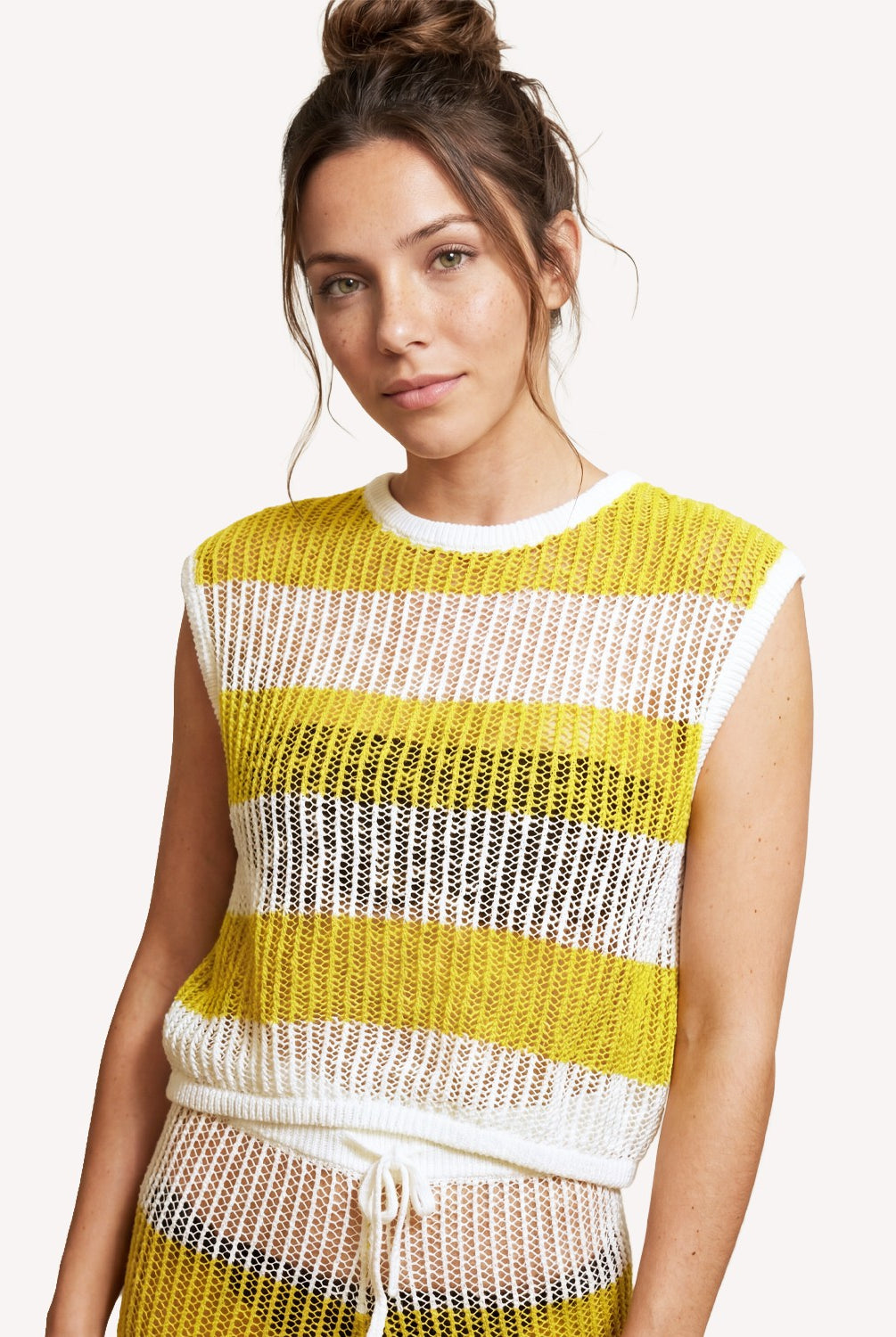Woman wearing a yellow and white striped sleeveless top on a plain background