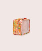 A packing cube with an orange floral print against a white wall.