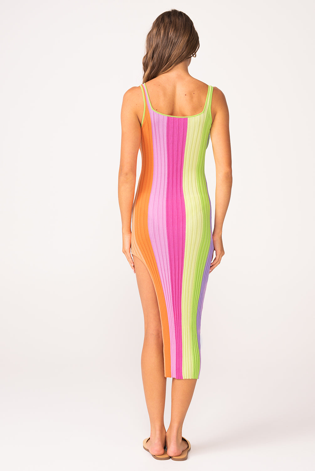A woman wearing a colorful striped dress facing towards a white wall.