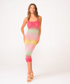 A woman wearing a pink, green, and yellow crochet knit mid length dress in front of a white background.