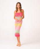 A woman wearing a pink, green, and yellow crochet knit mid length dress in front of a white background.