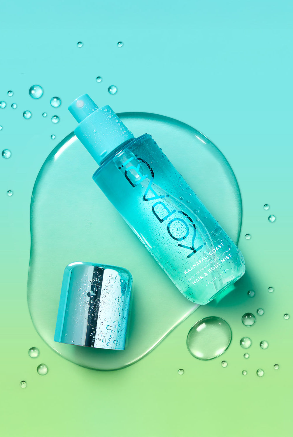 The Kopari Creamy Coconut Hair & Body Mist bottle lying on a wet blue and green background with the cap off.