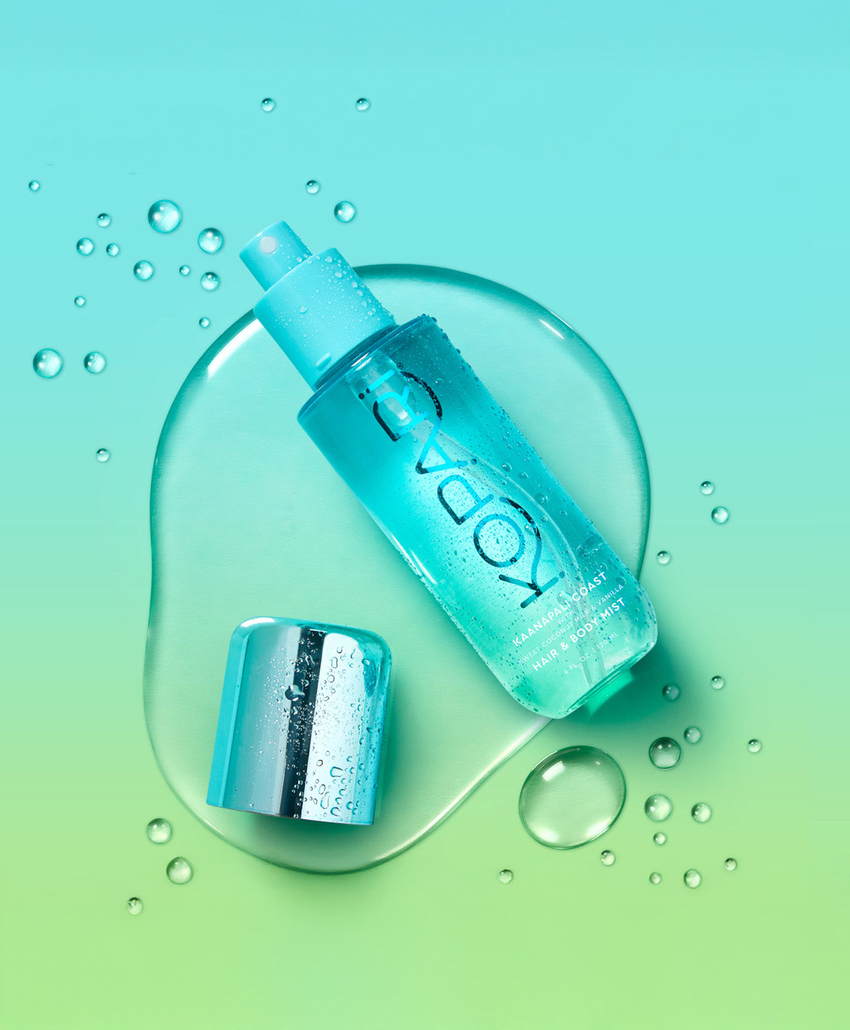 The Kopari Creamy Coconut Hair & Body Mist bottle lying on a wet blue and green background with the cap off.