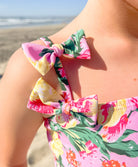 A young girl wearing a colorful floral one piece suit with a bow on a beach