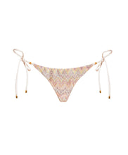 A multi-colored print triangle bikini bottom with gold details. Featured against a white wall background.