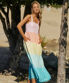 A blonde woman wearing a long multi colored dress standing near trees.