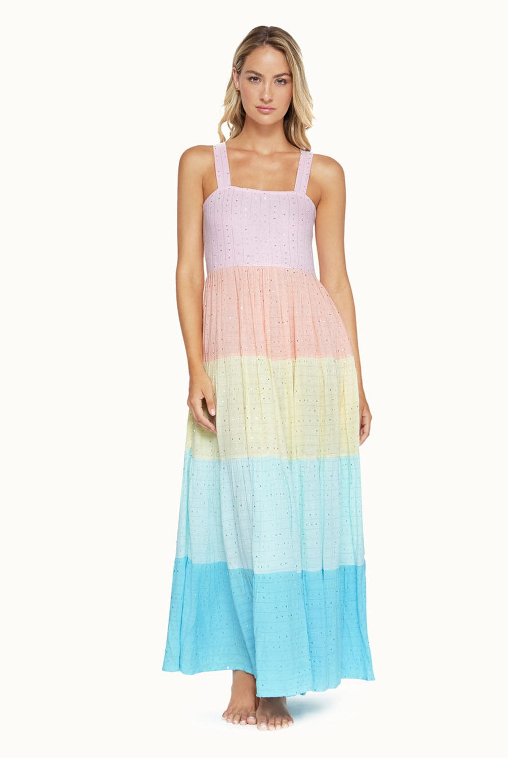 A blonde woman wearing a multi colored dress standing in front of a white wall.