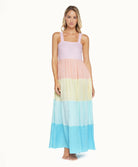 A blonde woman wearing a multi colored dress standing in front of a white wall.