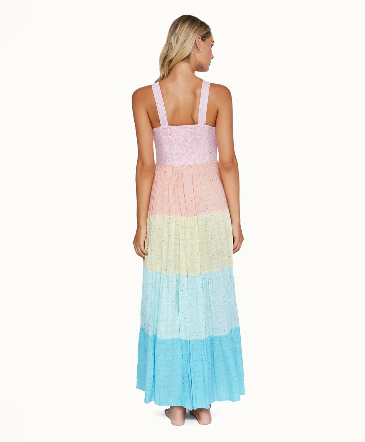 A blonde woman wearing a multi colored dress facing towards a white wall.