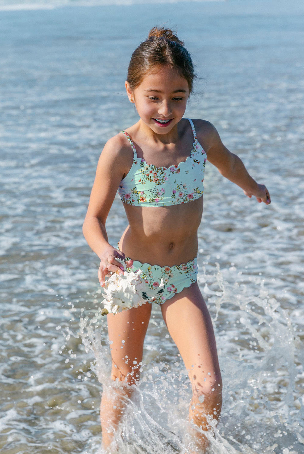 Young girl in a floral swimsuit playing in the ocean.