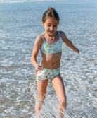 Young girl in a floral swimsuit playing in the ocean.