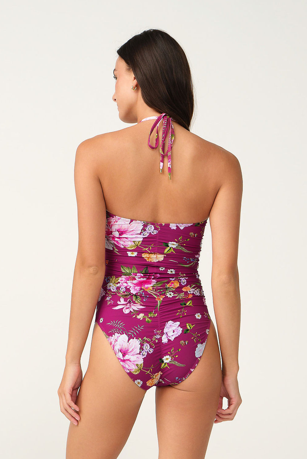 A woman shown from the back wearing a floral one-piece swimsuit with a halter-style neck and tie, against a plain light background.