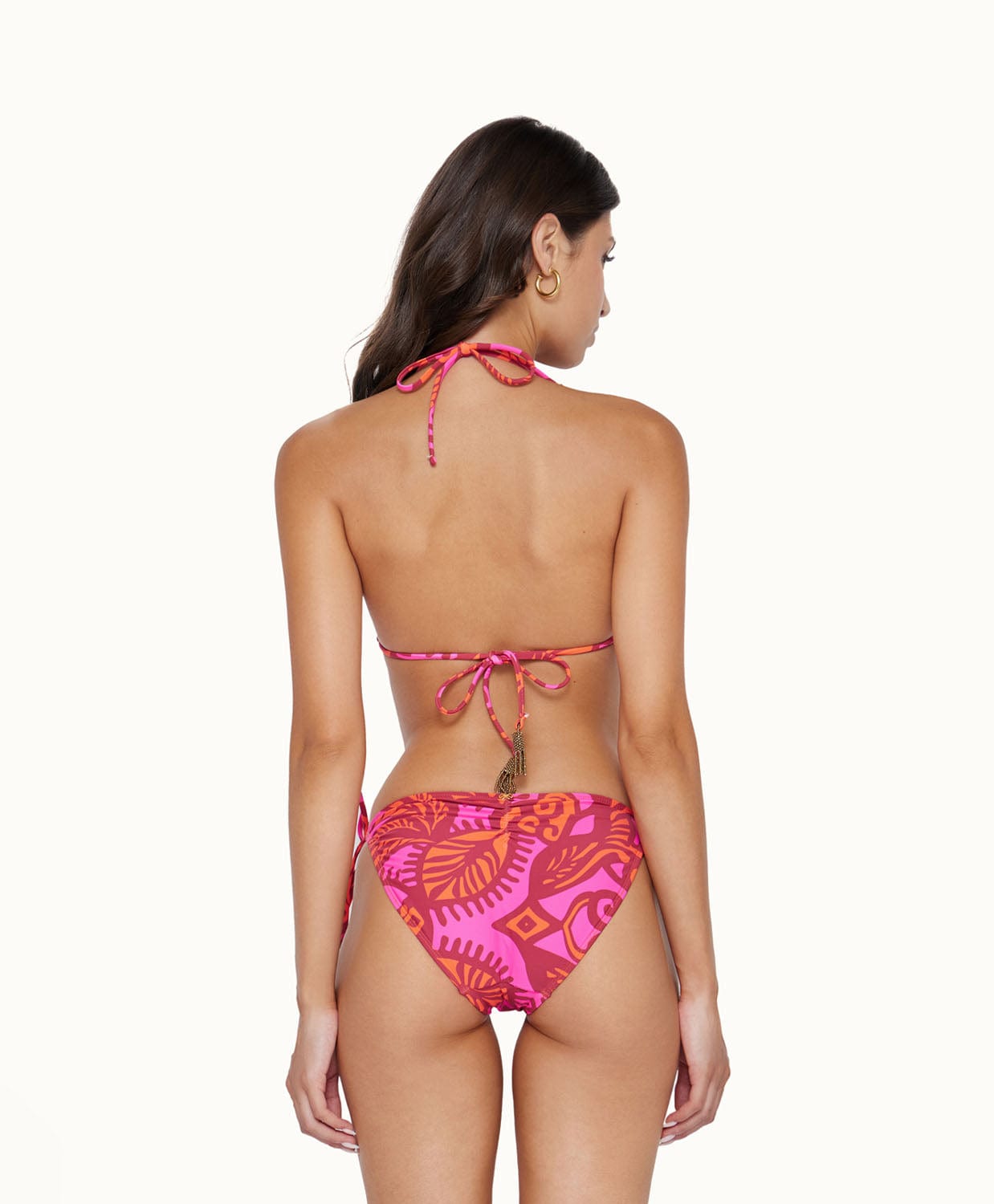 A brunette woman wearing a pink and red bikini facing towards a white wall.