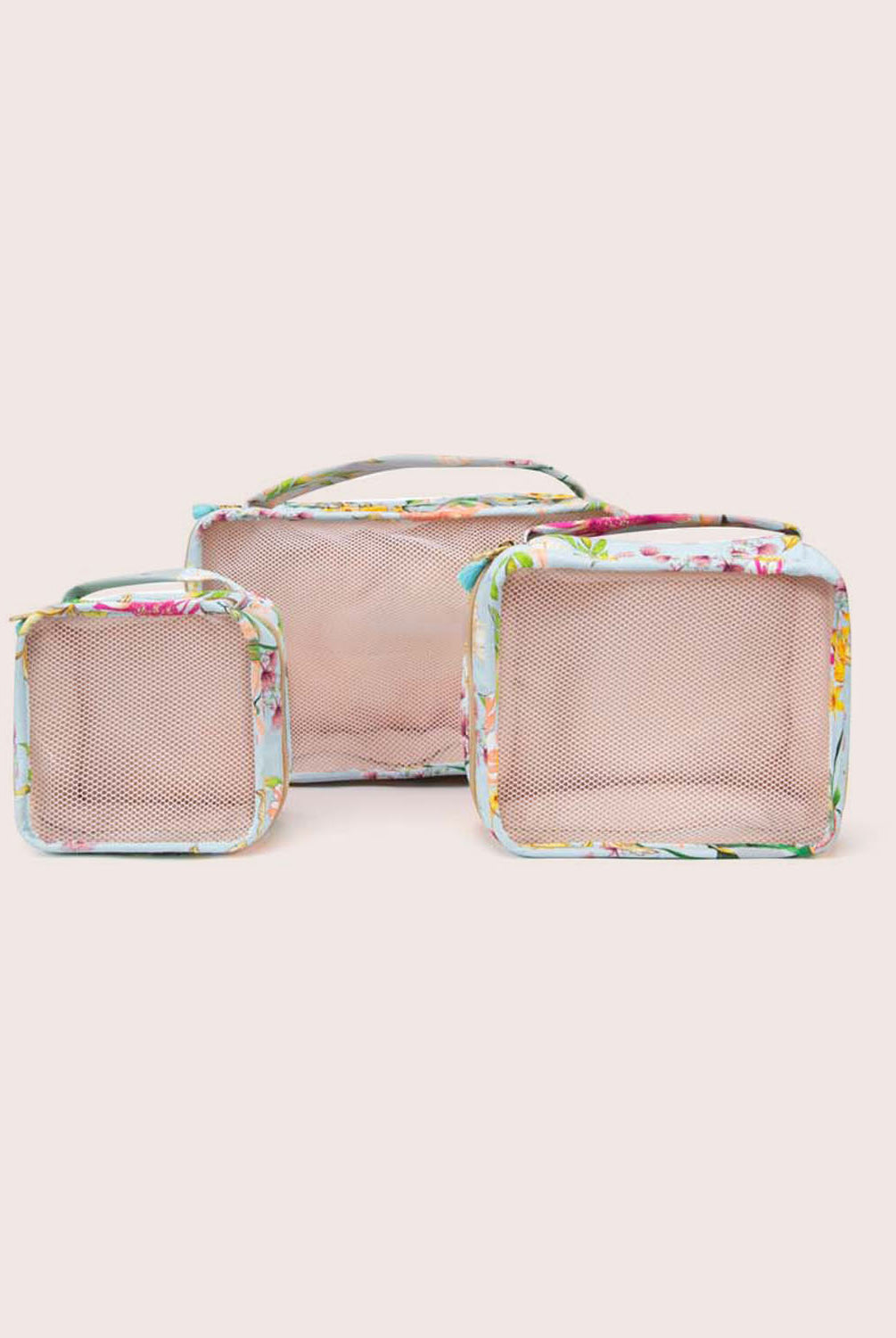 A set of three packing cubes against a white wall.