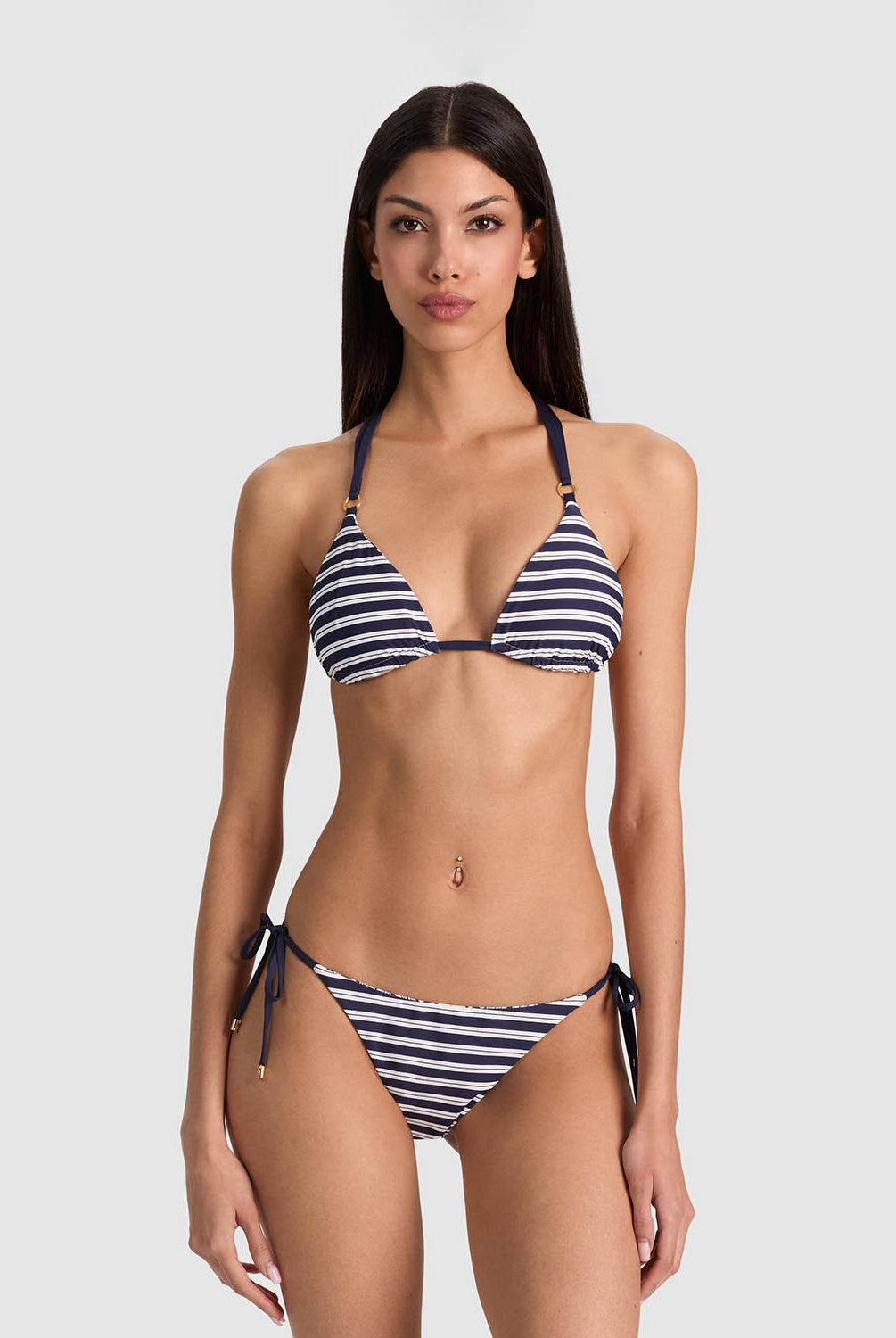 A woman modeling a navy and white striped triangle bikini with side-tie bottoms against a light gray studio background.