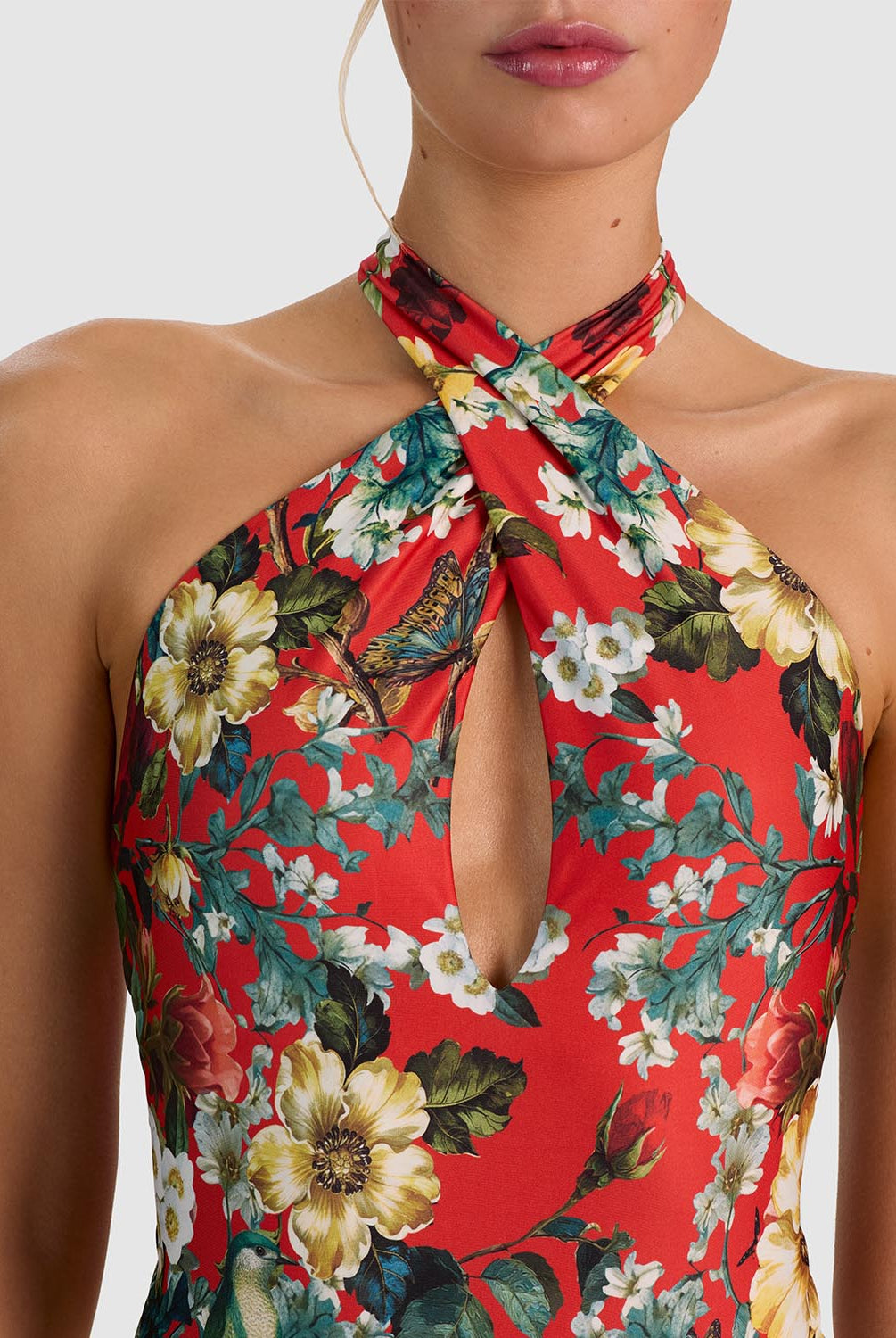 A close-up of a model wearing a red halter-neck dress with a vibrant floral print featuring yellow, white, and green flowers.