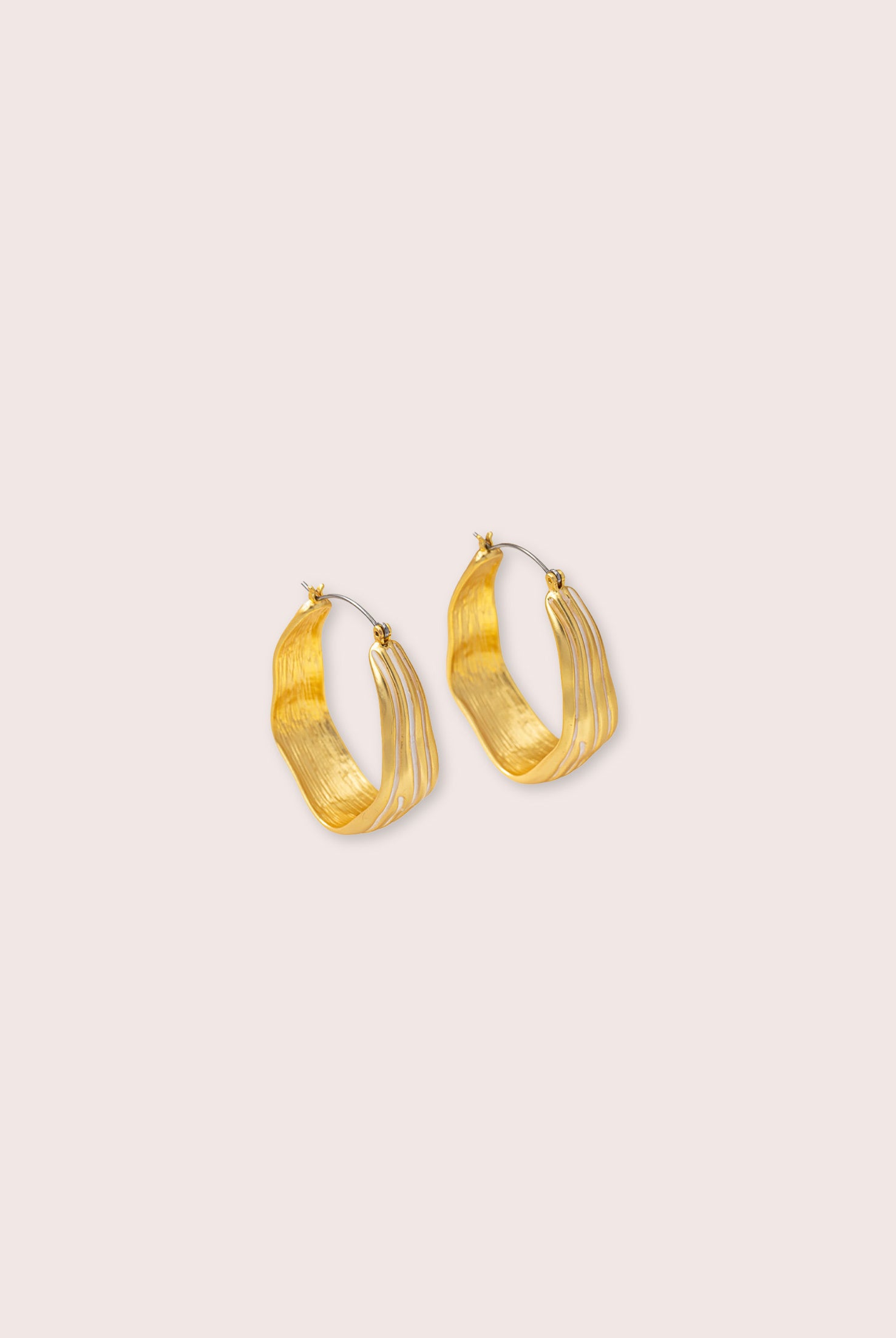Gold hoop earrings against a white wall.