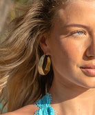 A woman wearing a teal bikini top and gold hoop earrings standing outside near palm trees.