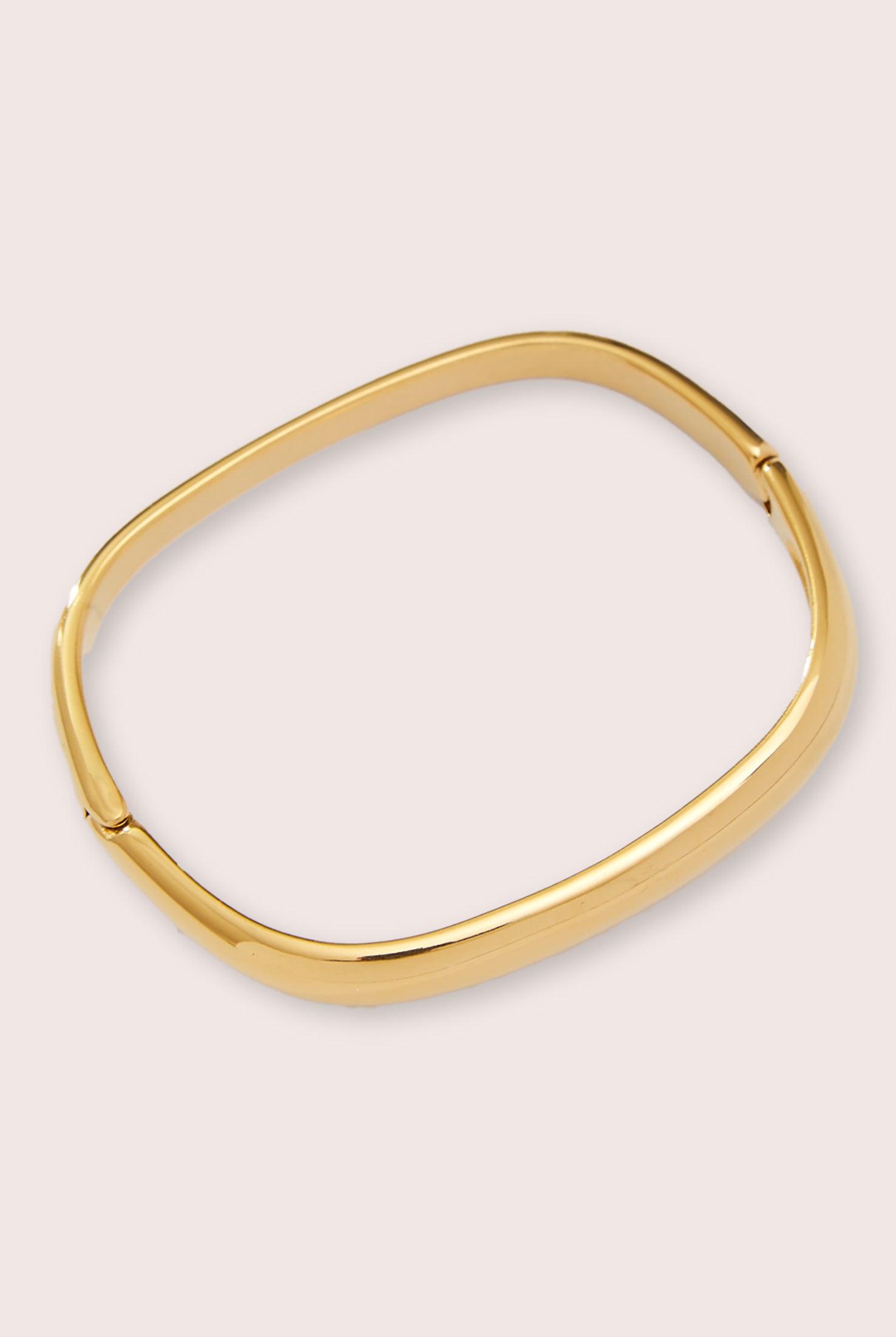 A gold square bracelet against a white wall.