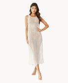 Brunette woman wearing an ivory sleeveless cover up with scalloped lace detailing stands in front of white wall.