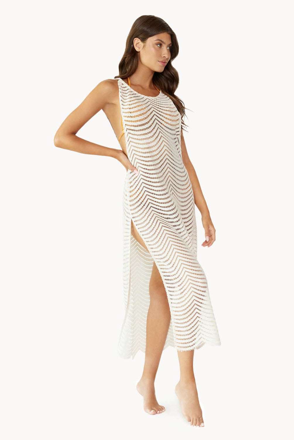 Brunette woman wearing an ivory sleeveless cover up with scalloped lace detailing stands in front of white wall.