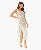 Brunette woman wearing an ivory sleeveless cover up with scalloped lace detailing stands in front of white wall.