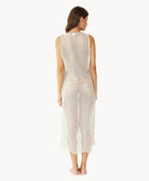 Brunette woman wearing an ivory sleeveless cover up with scalloped lace detailing facing backwards towards white wall.