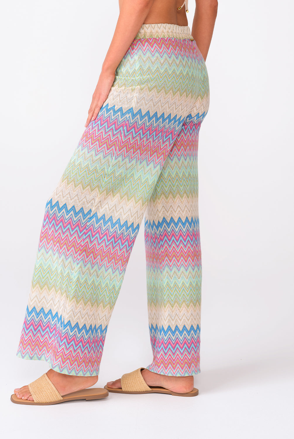 A woman wearing colorful striped pants standing against a white wall.