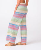 A woman wearing colorful striped pants standing against a white wall.