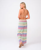 A woman wearing a striped triangle top and matching pants facing towards a white wall.