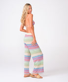 A woman wearing a striped triangle top and matching pants against a white wall.