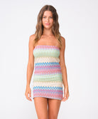 A woman wearing  a colorful striped mini dress standing against a white wall.