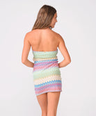 A woman wearing  a colorful striped mini dress standing against a white wall.