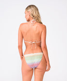 A woman wearing a multi colored striped bikini standing against a white wall.