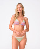 A woman wearing a striped triangle top and matching bottoms standing against a white wall.