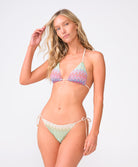 A woman wearing a striped triangle top and matching bottoms standing against a white wall.