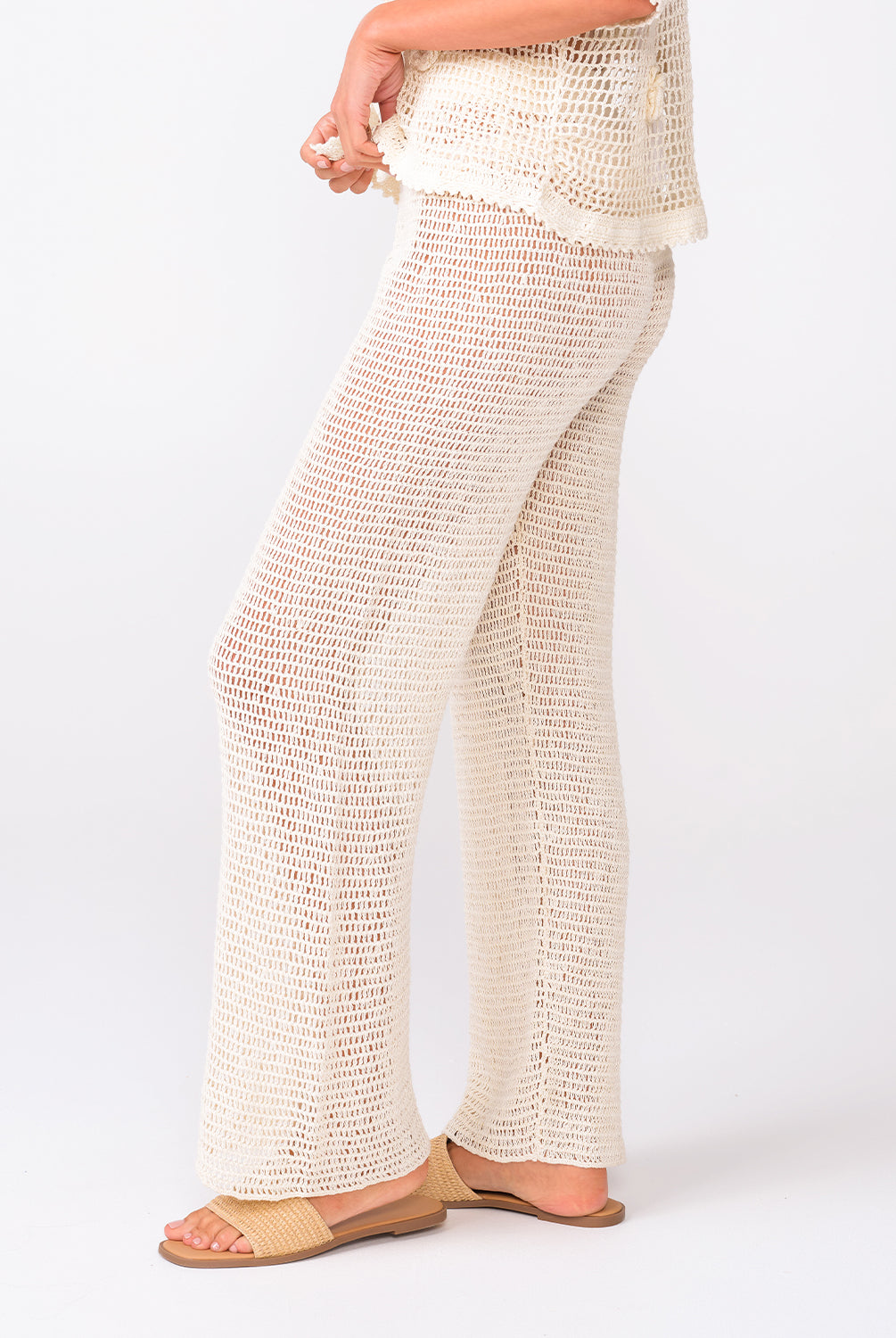A woman wearing ivory knit pants standing against a white wall.