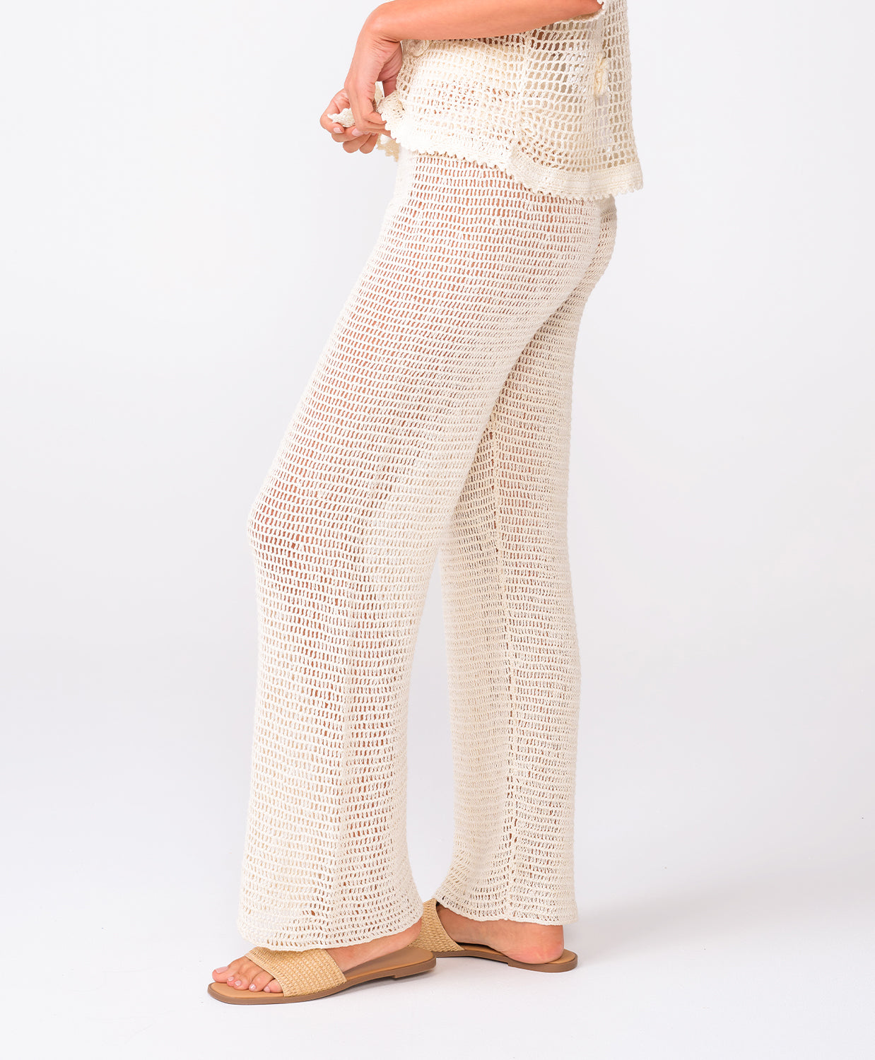 A woman wearing ivory knit pants standing against a white wall.