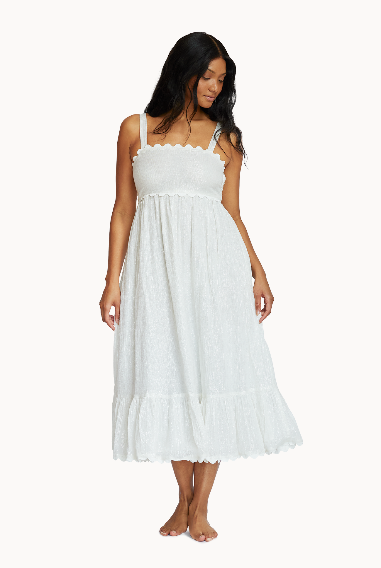 A woman wearing a midi length white dress standing in front of a white wall.