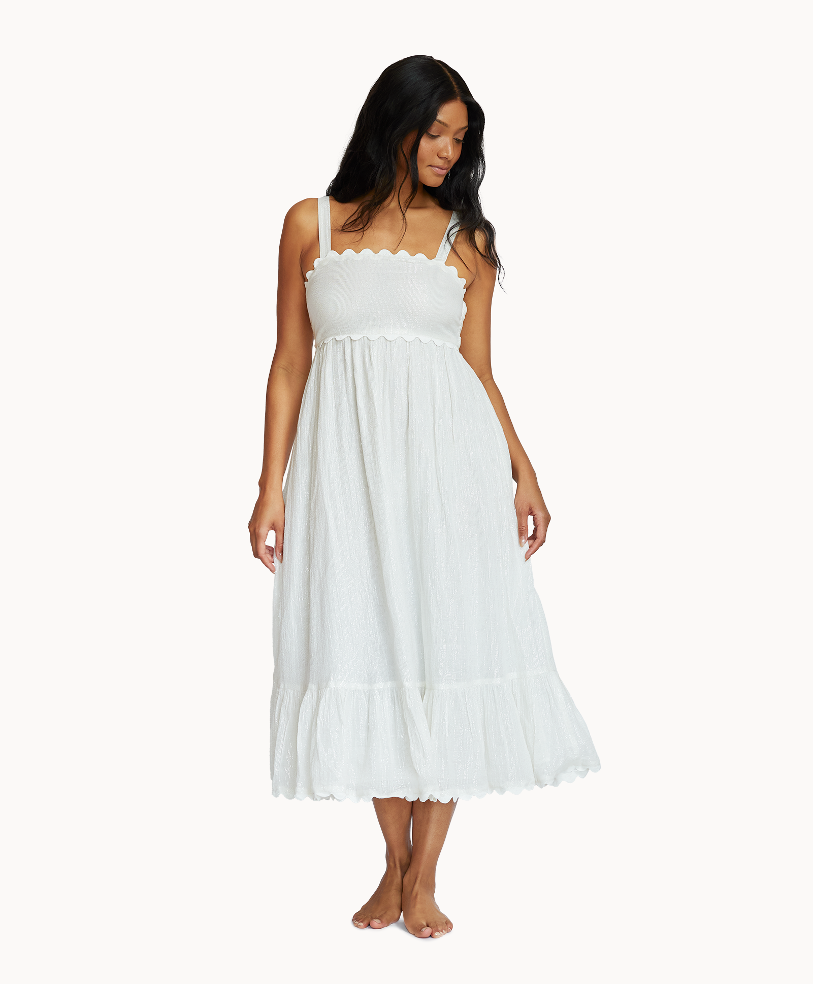 A woman wearing a midi length white dress standing in front of a white wall.