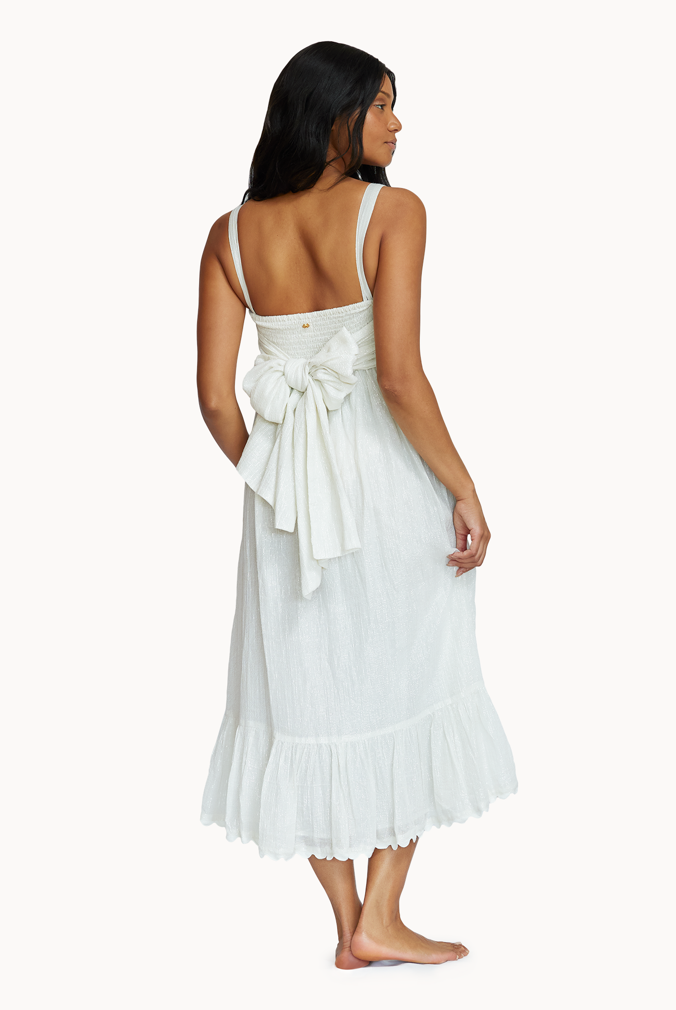 A woman wearing a midi length white dress acing towards a white wall.