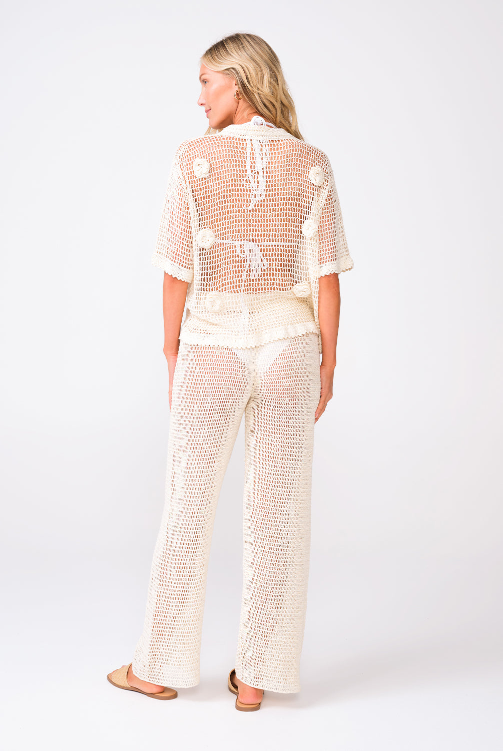 A woman wearing an ivory knit shirt and matching pants standing against a white wall.
