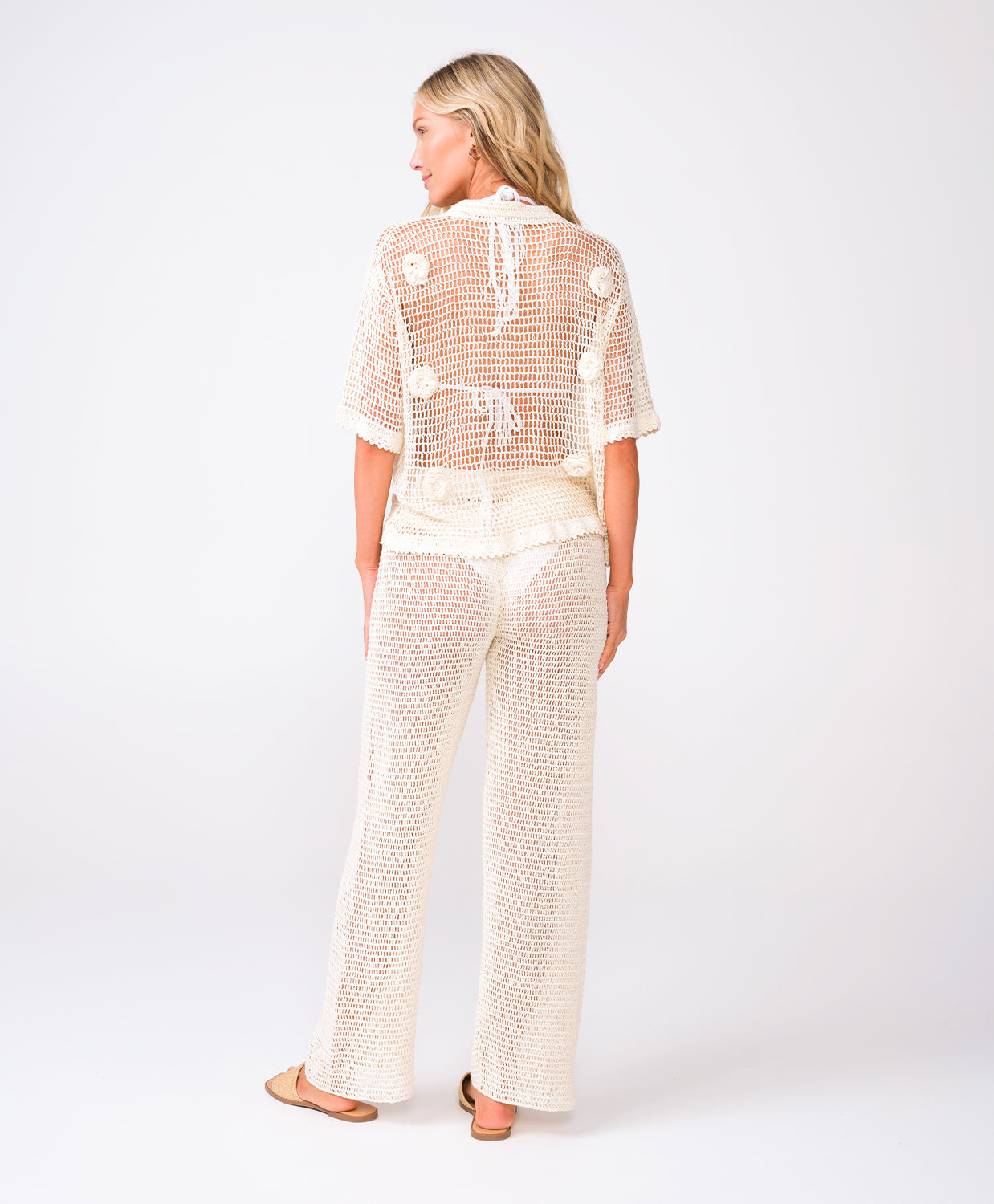 A woman wearing an ivory knit shirt and matching pants standing against a white wall.